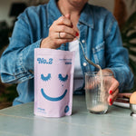Person sitting at a breakfast table spooning No.2 Good Gut FIbre with a blend of psyllium husk powder collagen into a glass.