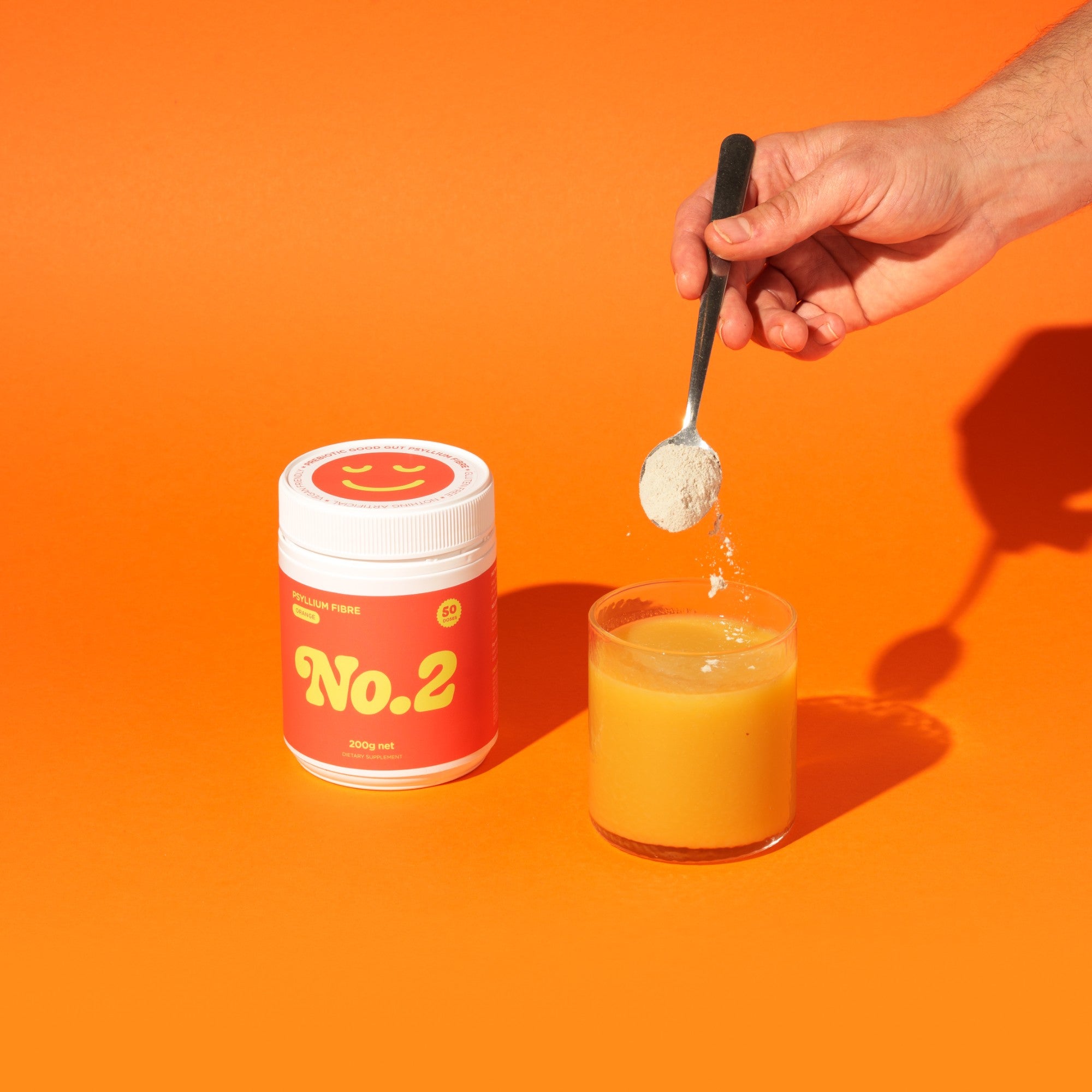 A hand sprinkling No.2 Good Gut Fibre in Orange Juice